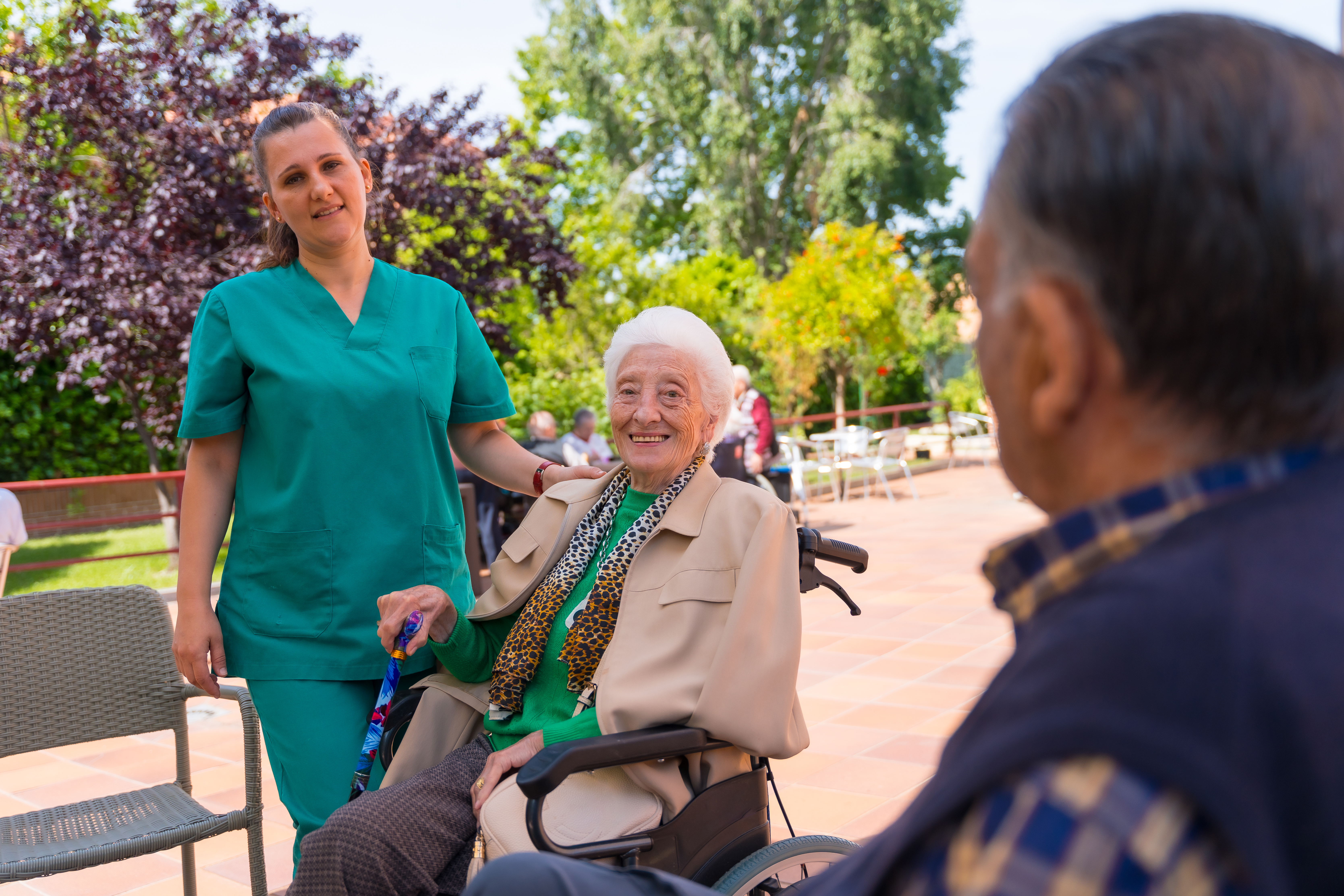 Portrait of an elderly woman with the nurse in the wheelchair in the garden of a nursing home